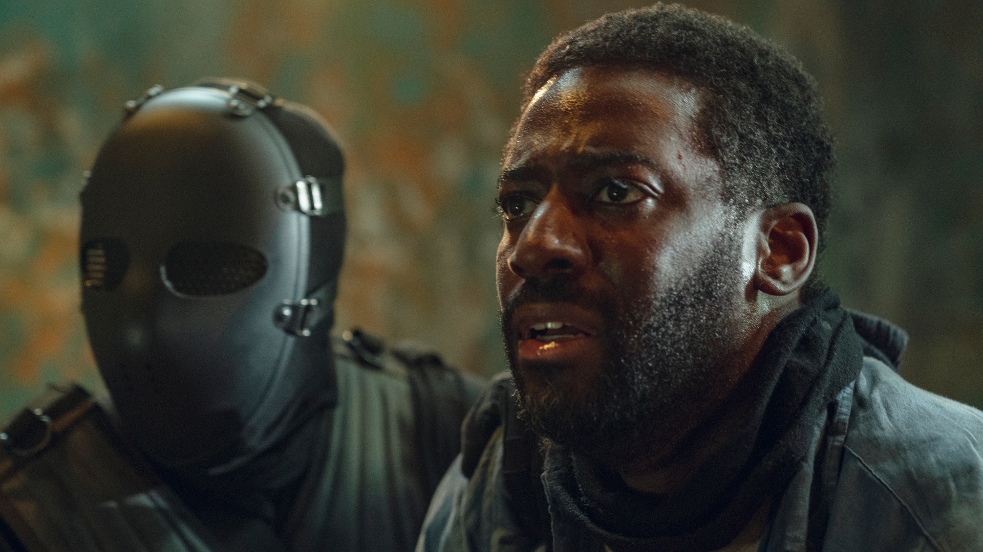 Alex sits next to a masked gunman in Hostage