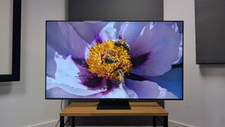 TCL C855K 65-inch Mini LED TV on wooden AV bench with flower on screen