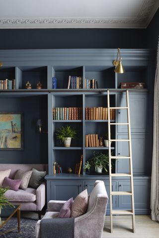 Home library with blue shelving and ladder, sofa and armchair
