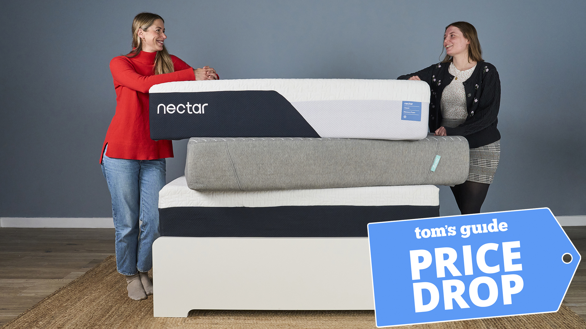 Two mattress testers stand either side of a stack of memory foam mattresses, including the Nectar Classic and Siena, on a bed frame. A Tom's Guide Price Drop deals graphic in the bottom right corner