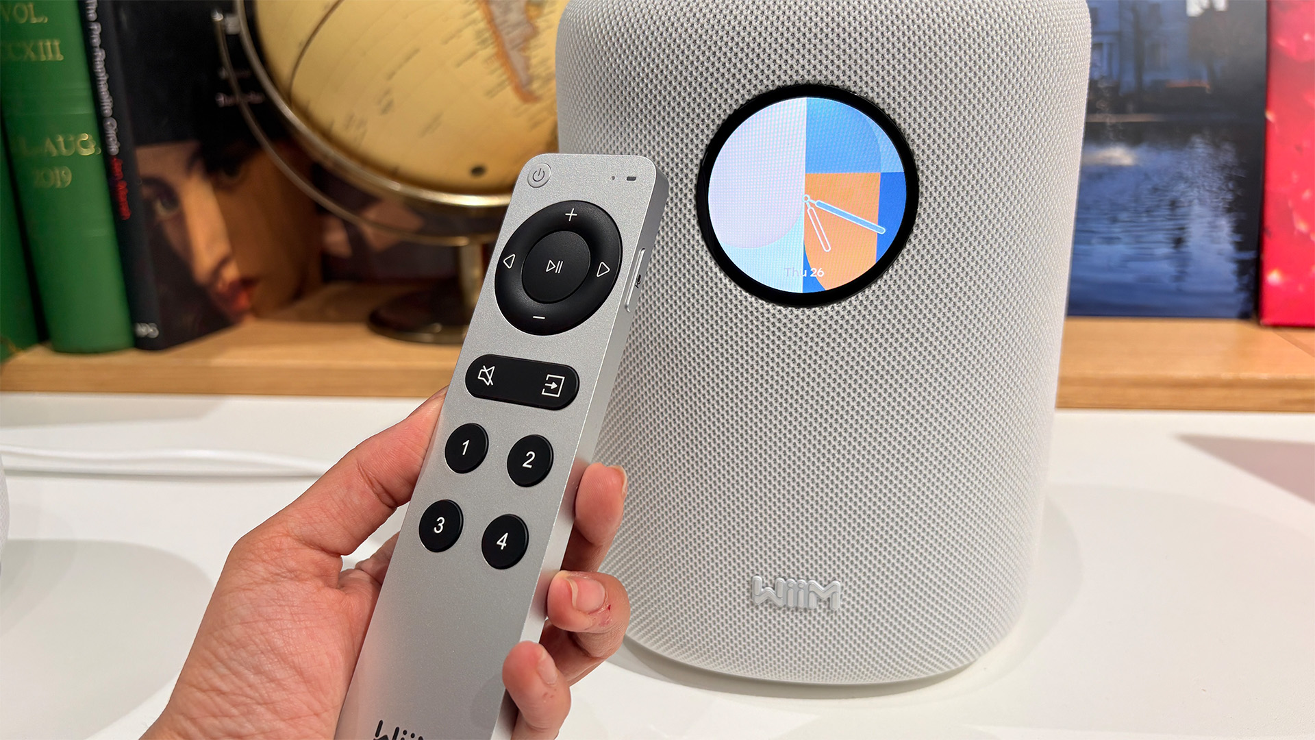 WiiM Sound wireless speaker in white with remote control held in hand