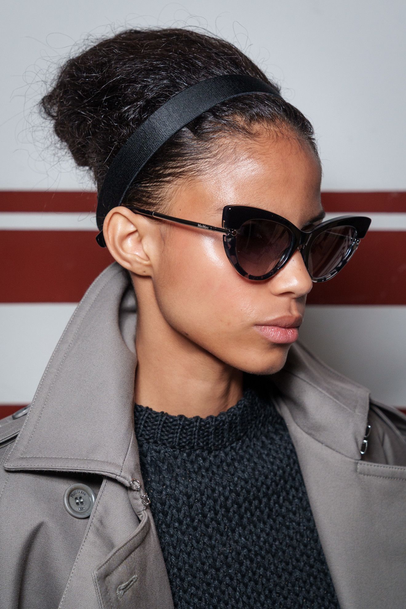 A model at the SS26 Max Mara show wearing a trench coat and sunglasses with a voluminous updo hairstyle