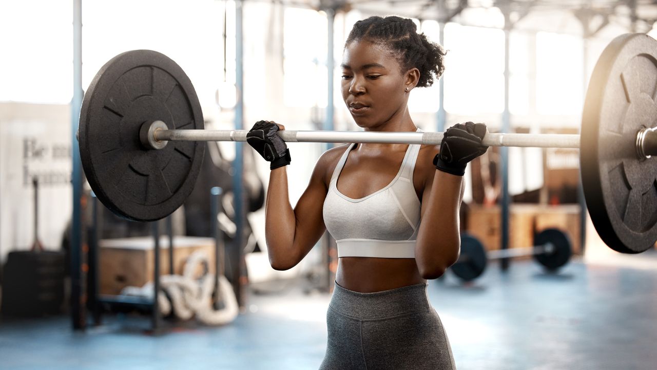 Shot of a sporty young woman exercising with a barbell in a gym