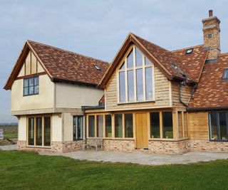 Traditional-style oak and timber frame self build, with render and timber clad exterior and clay roof tiles. The self build features a large glazed pitched elevation.