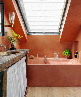 Orange painted walls in attic bathroom with orange coloured bath tub and wooden floorbords and wooden sink unit