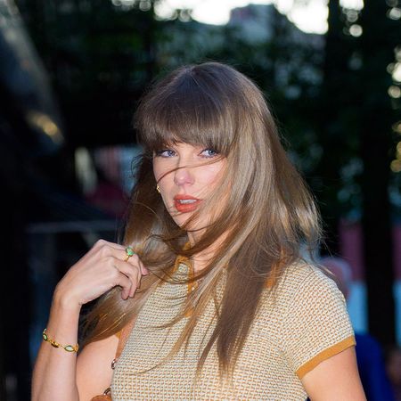 Taylor Swift wearing a beige cashmere polo shirt, blue jeans, tan belt, tan shoulder bag, and tan Gucci sandals
