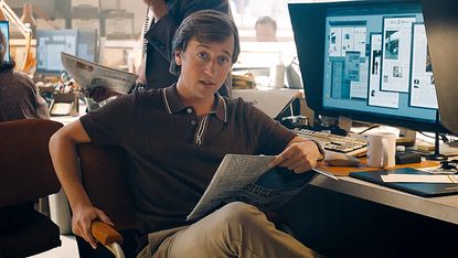 Jimmy Olsen sitting at his Daily Planet desk and holding a newspaper in 2025's Superman movie