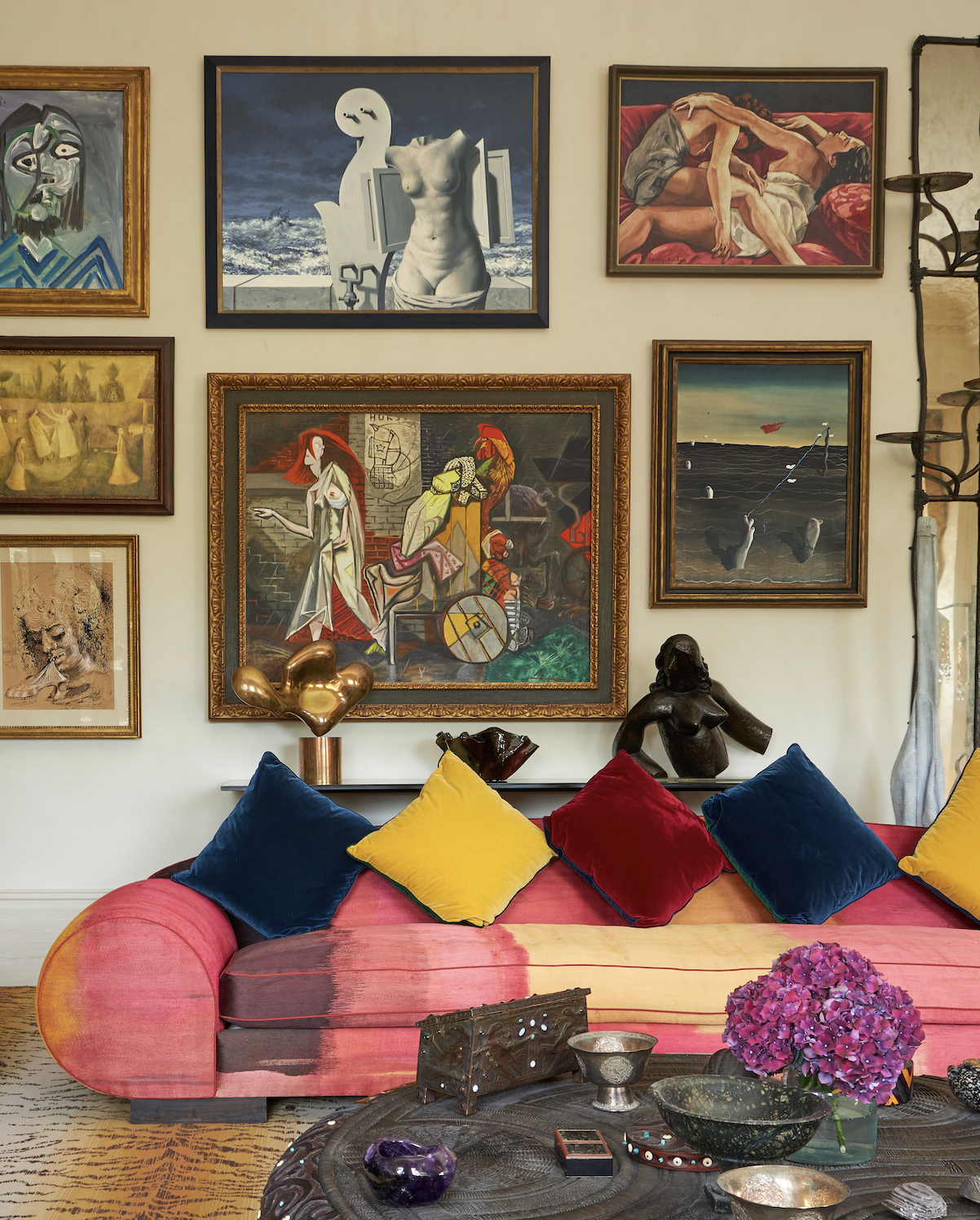 Inside the apartment a pink and yellow sofa stacked with blue, yellow and red pillows stands in front of works of art.