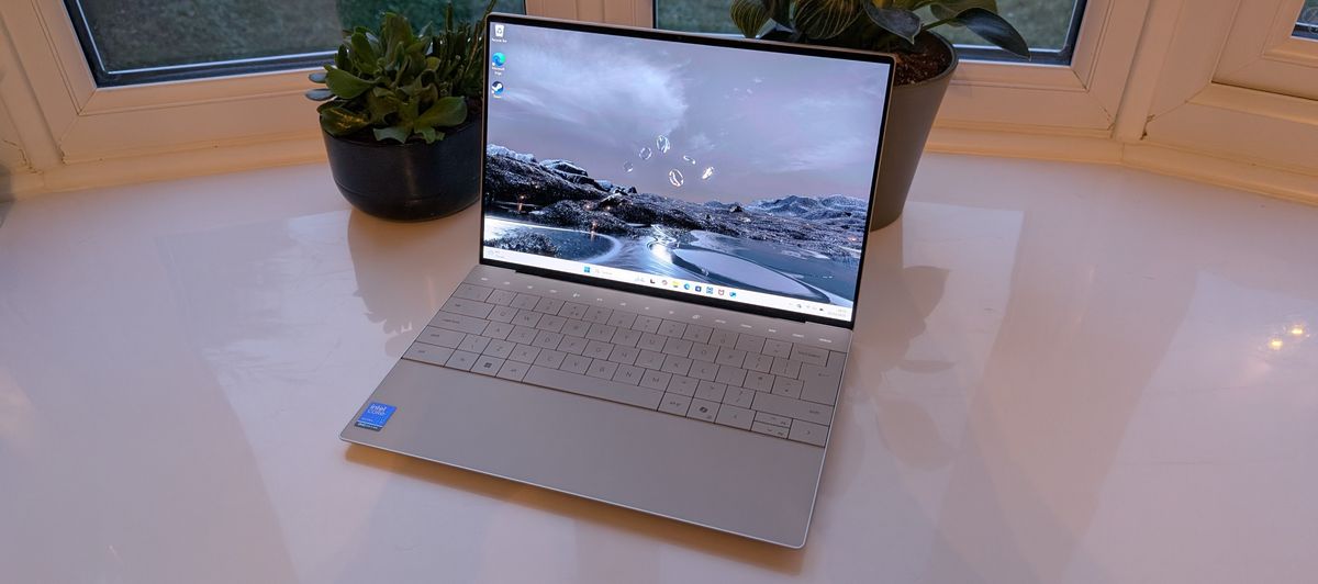 The Dell XPS 13 pictured on a white surface in front of a window with two potted plants.