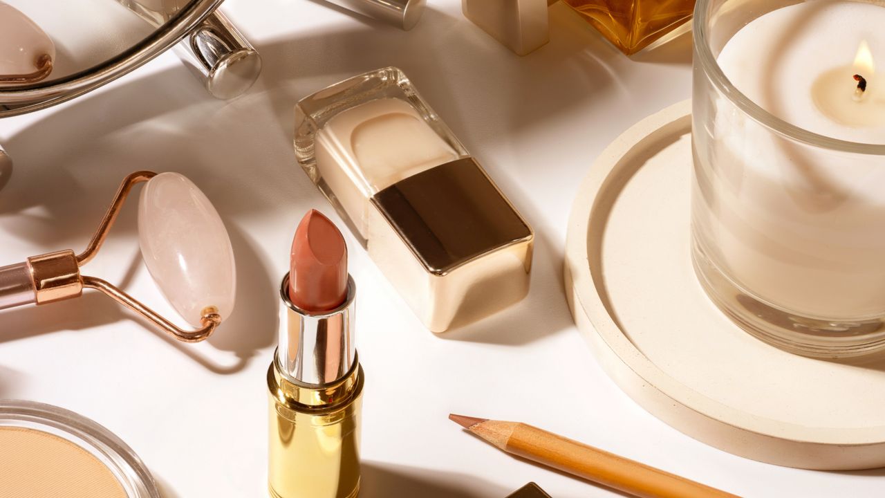 A selection of make-up, beauty tools and a candle laid out on a white surface 