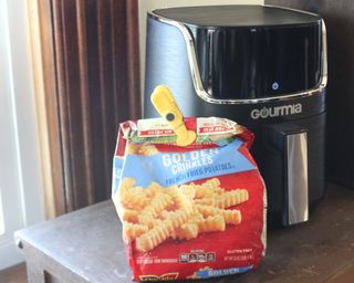 A bag of frozen french fries with Gourmia 4-quart digital air fryer on wooden table