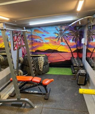 A home gym set up in a garage with spray painted wall art on garage door