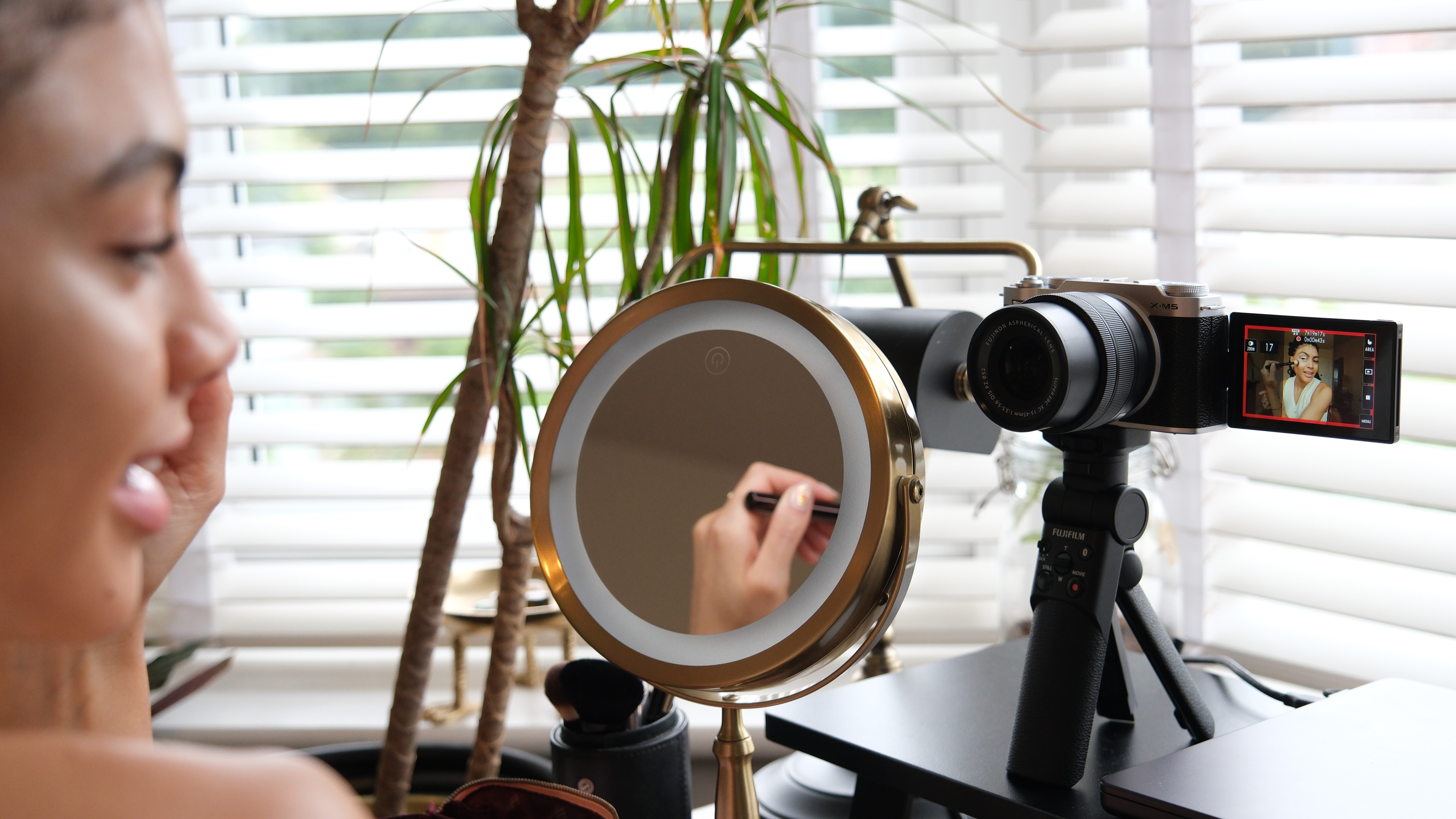 Une personne devant un miroir de maquillage, se filmant en train de se maquiller sur un appareil photo Fujifilm X-M5