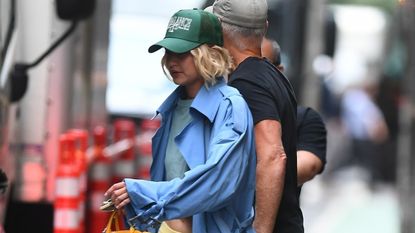 Gigi Hadid wearing a blue trench coat, butter yellow trousers, Birkenstocks, and a yellow Miu Miu bag in New York City July 2024