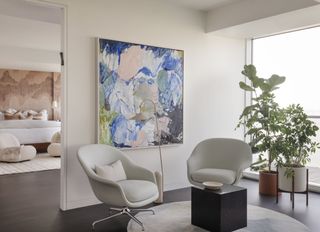 Seating area next to bedroom with white walls, chairs and colorful art