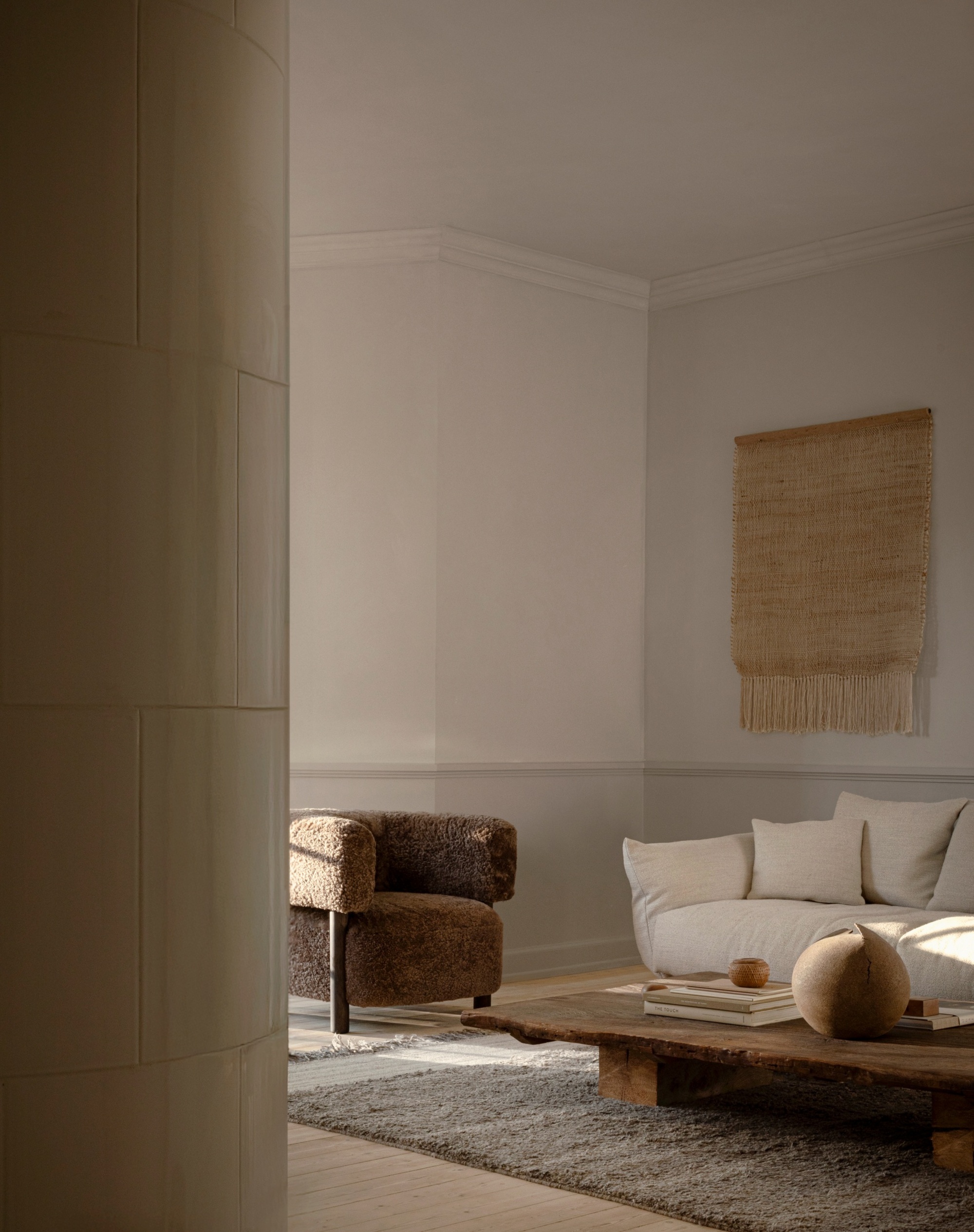 A Scandi living room with a low profile wooden coffee table, a shaggy brown accent chair, and a woven tapestry on the wall