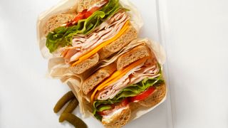 Layers of turkey meat with cheese and salad in a bagel with cornichons around the sides