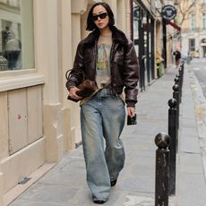 A woman wears baggy jeans, t-shirt, brown leathers bomber while walking the streets of Paris.