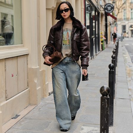 A woman wears baggy jeans, t-shirt, brown leathers bomber while walking the streets of Paris.