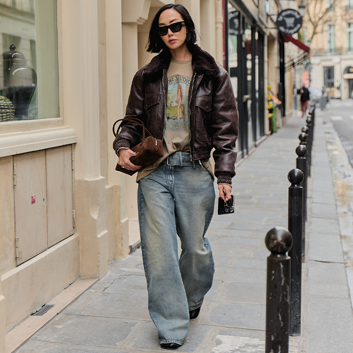 A woman wears baggy jeans, t-shirt, brown leathers bomber while walking the streets of Paris.