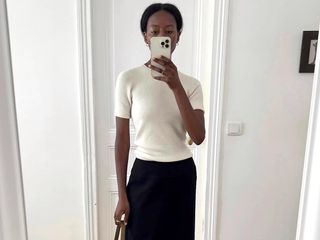 influencer Sylvie Mus poses for a mirror selfie wearing a cream short sleeve sweater top and black skirt