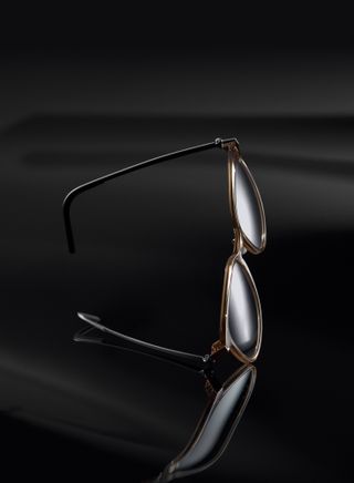 Black background, pair of sunglasses angled on a reflective surface