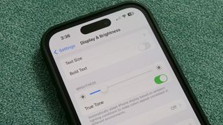 Display and Brightness menu on an iPhone 14 Pro sitting on a couch cushion