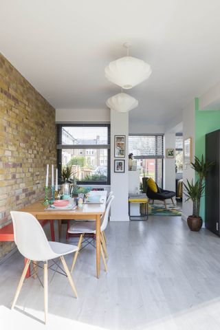 white open plan space with a brick effect wall, wooden fining table and a bright green feature wall