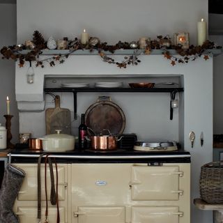 A kitchen with a cream stove and oven and a shelf decorated with an autumnal garland