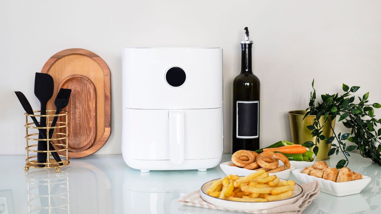 A white air fryer on a kitchen counter with silicone tools and fried foods 