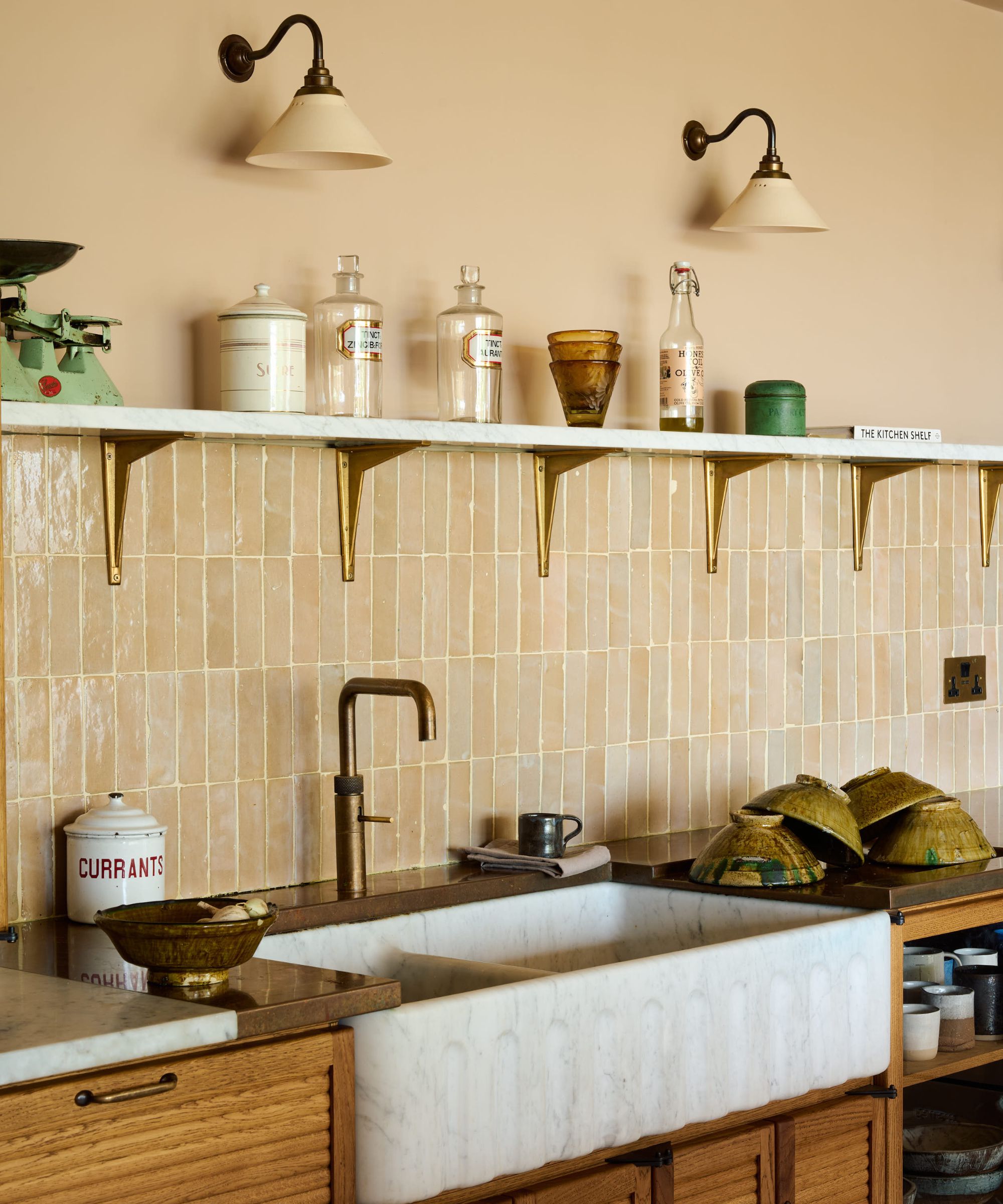A large kitchen sink with a tile kitchen backsplash, an open shelf decorated with ceramics, and a warm neutral paint color on the walls by Little Greene