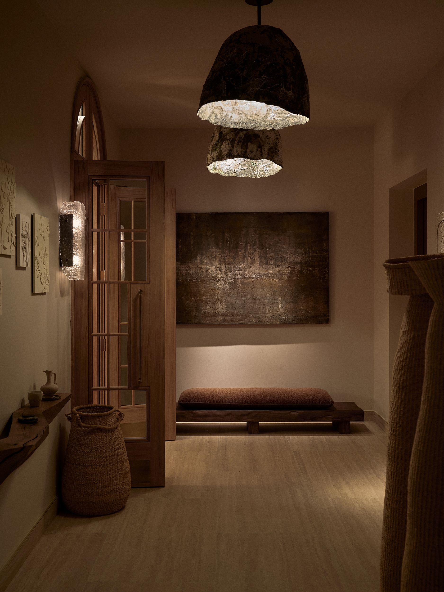 A hotel spa decorated with textile installations characterized by a textural, raw feel, sculptural tables carved from wood and rock, pendant lights, and a beige fabric-covered wall.