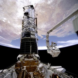 Astronaut F. Story Musgrave, anchored on the end of the Remote Manipulator System (RMS) arm, prepares to be elevated to the top of the Hubble Space Telescope (HST) to install protective covers on the magnetometers during Endeavour's STS-61 mission, which