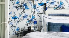 Blue, white, and black bedroom with patterned wallpaper, black bed, white bedding, blue cushions, black nightstand, and a white open door to the left.