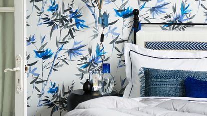 Blue, white, and black bedroom with patterned wallpaper, black bed, white bedding, blue cushions, black nightstand, and a white open door to the left.