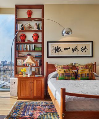 A bedroom with floor-to-ceiling windows, built-in wooden shelving and a colorful area rug