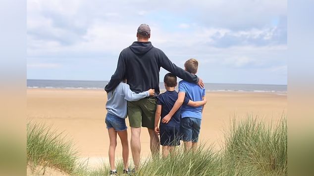 The Prince of Wales and his three children from behind, standing on a beach, taken by Kate Middleton