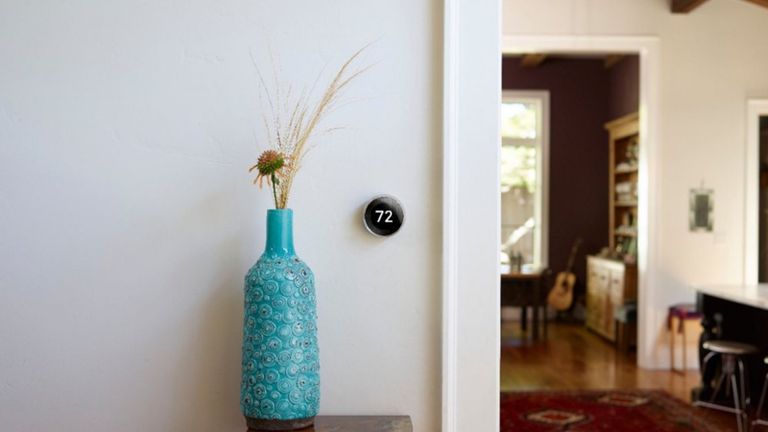 best smart thermostat Google Nest Learning Wi-Fi Thermostat mounted to wall beside blue vase