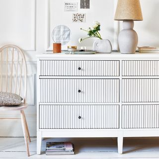 White chest of drawers with fluted design, decorative accessories, table lamp