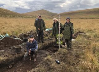 Four people stand in the English moorland at an excavation site