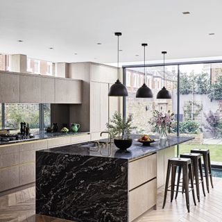 Modern fitted kitchen with grey wood-effect walls and black marble kitchen island on parquet floor