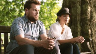 James Corden in a blue top as Jamie and Melia Kreiling in a white top and black cap as Amandine look tense on a bench in Mammals