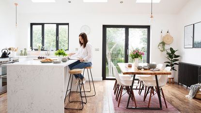 An open-plan kitchen diner with white units wooden flooring and black framed windows