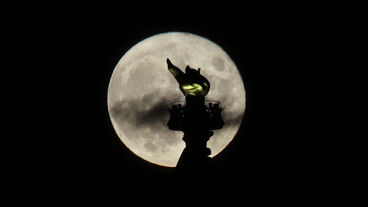The full Sturgeon Blue Moon rises behind the torch of the Statue of Liberty in New York City on Aug. 22, 2021 as seen from Jersey City, New Jersey.