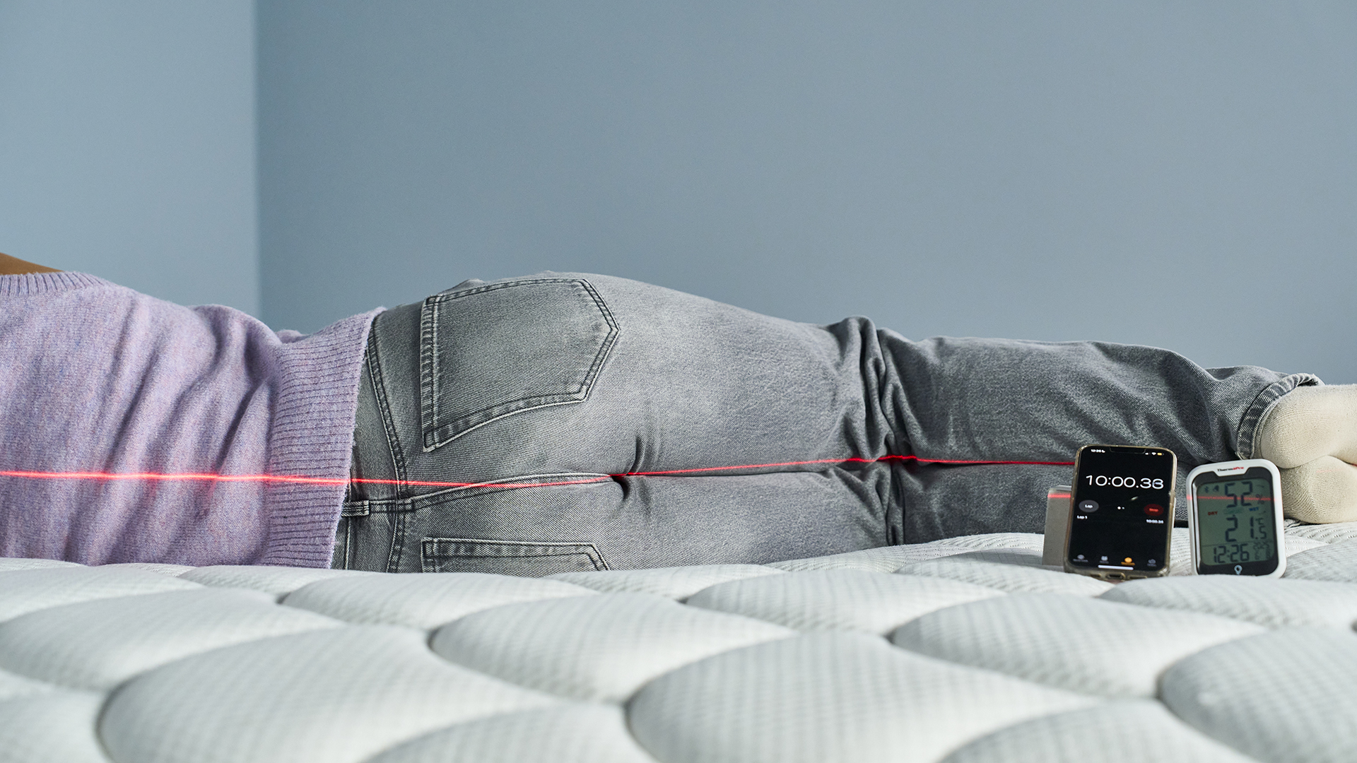 A Tom's Guide Tester lies on her side on the DreamCloud Classic mattress. A red line from a laser is seen along the side of her body to measure how straight her spine is.