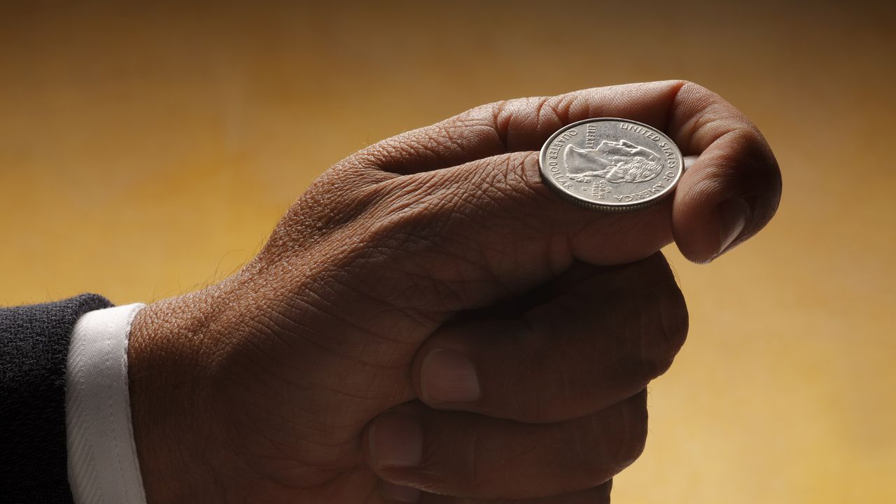 A quarter sits on the thumb of a man who&#039;s about to flip it.