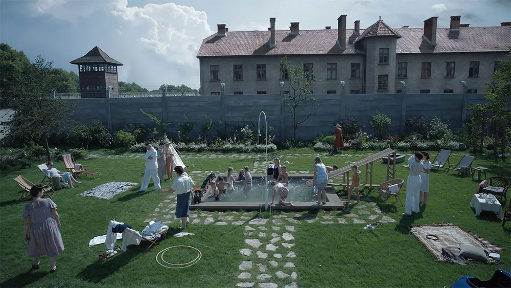 A shot of a garden with people in a small pool in the middle. In the background is a large building and a watchtower.