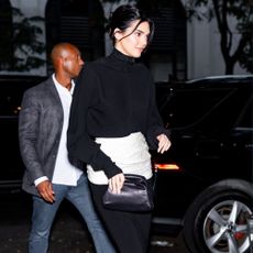 Kendall Jenner walks outside wearing a black knit, black midi skirt and mid-heel pumps.