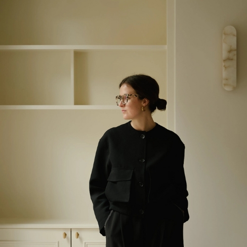 Image of a woman in an all-black outfit standing in front of a butter yellow background.