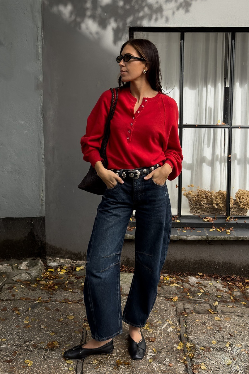 a woman wearing a red cardigan sweater, blue indigo jeans, black flats and brown woven leather bag